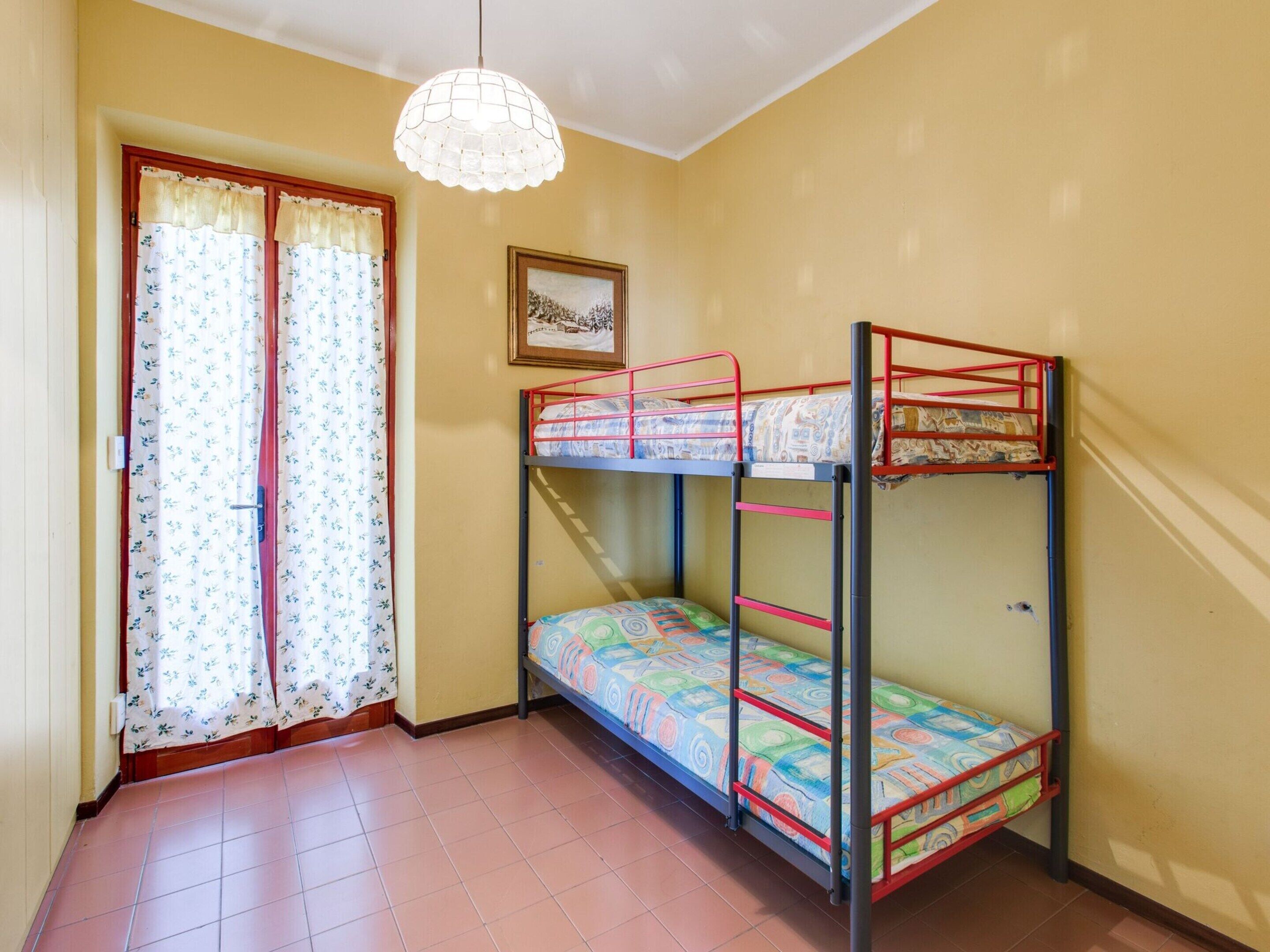 A room with bunk beds, a window with curtains, a framed picture on the wall, and a hanging light fixture.