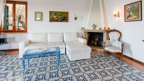 Ein Wohnzimmer mit einem weißen Sofa, einem blauen Couchtisch, einem gemusterten Boden, einem Kamin und einem gerahmten Gemälde an der Wand.
