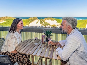 A couple seated at a wooden table with a view of the beach and dunes. - 4 Person Holiday Park Home in Blokhus (Blokhus)
