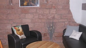 A room with a brick wall, a framed picture, two leather chairs, a wooden table, and a vase with dried flowers. - Chez Emil and Isabelle (Rumbach)