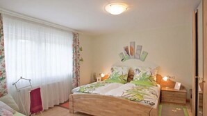 A bedroom with a wooden bed, a nightstand, a bedside table, a mirror, a window with sheer curtains, and a wooden floor. - Chez Emil and Isabelle (Rumbach)