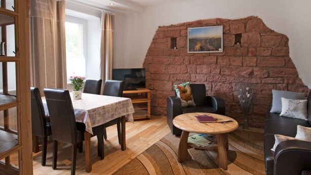 A cozy living room with a stone wall, a dining area with a table and chairs, and a comfortable seating area with a sofa and armchairs. - Chez Emil and Isabelle (Rumbach)
