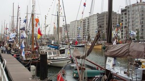 A marina with multiple sailboats docked, surrounded by buildings. - Schmitz Comfortable Holiday Residence (De Haan)
