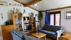 A living room with a sofa, a coffee table, a TV, and a wooden cabinet. - Schmitz Comfortable Holiday Residence (De Haan)