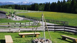 A rustic outdoor setting with a wooden swing, picnic tables, and a fenced area with a mountain backdrop. - Characteristic Apartment in Bernbeuren (Bernbeuren)