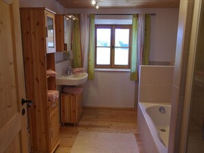 Een houten badkamer met een houten wastafel, een wastafel, een spiegel, een raam met gordijnen en een bad.