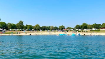 A lakeside beach with boats, tents, and people.