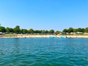 A lakeside beach with boats, tents, and people.