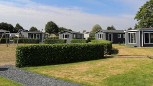 A row of mobile homes with a grassy lawn and a hedge in the foreground. - Chalet on the Recreational Lake and the Veluwe (Lathum)