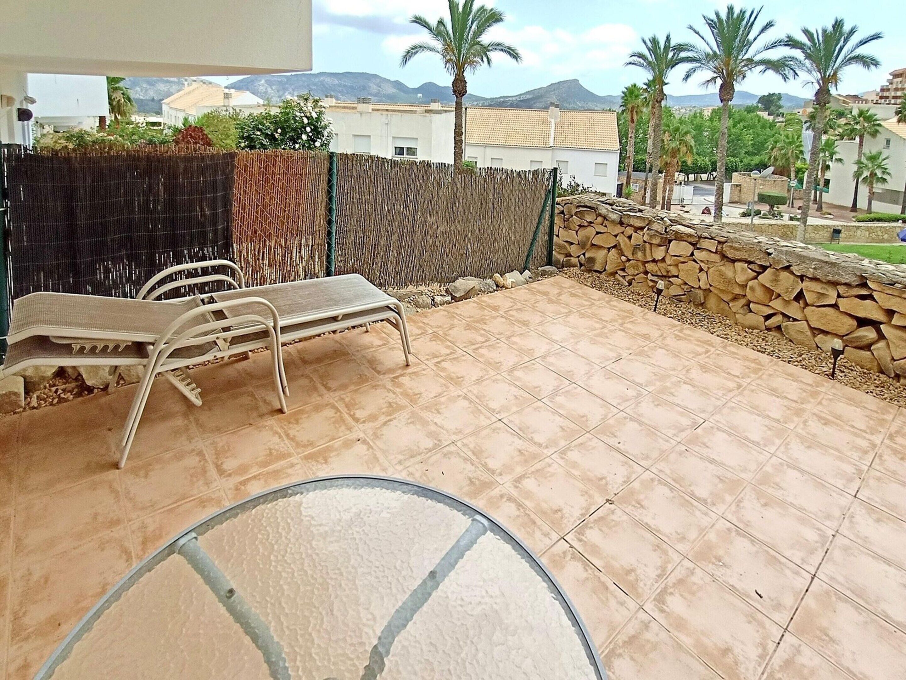 A patio with a metal table and chairs, a stone wall, and a view of palm trees and buildings in the background.
