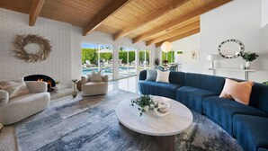 Ein geräumiges Wohnzimmer mit Kamin, Blick auf einen Pool und einem modernen, blauen Sofa.