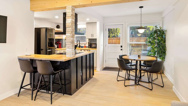 A modern kitchen with a central island, bar stools, and a dining area with a round table and chairs. - Cute 3BR/2BA w/ Jacuzzi, Steps from Big House! (Ann Arbor)