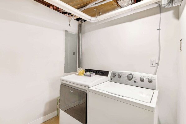 A laundry room with a washer and dryer, a white wall, and visible plumbing.