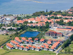An aerial view of a coastal residential area with red-roofed houses, a small lake, and a church spire.