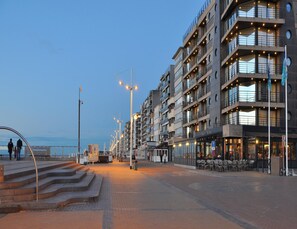 A waterfront promenade with modern buildings, outdoor seating, and a clear sky. - Apartment on Zeedijk With Stunning Sea View (Koksijde)