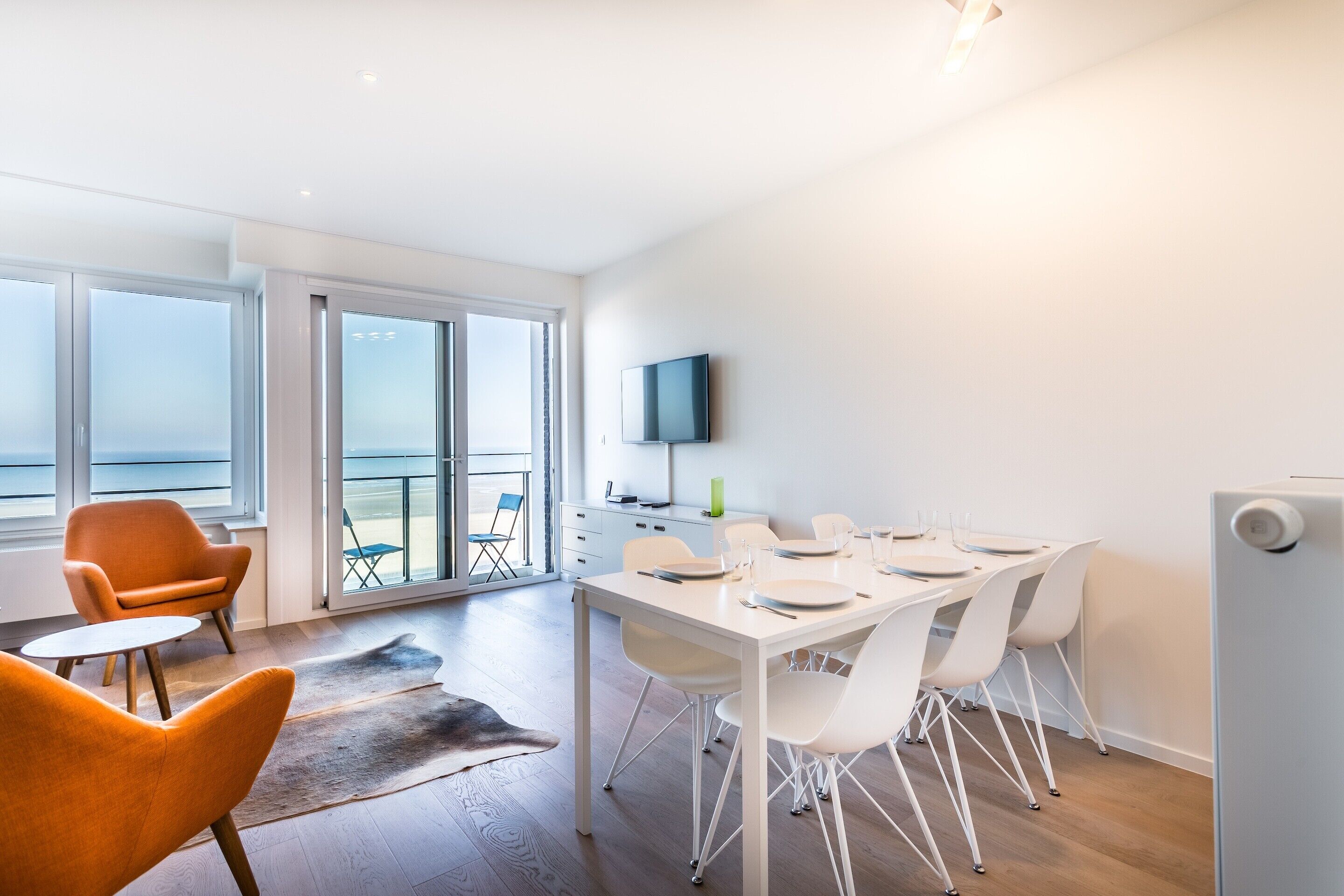 A modern dining area with a table set for four, white chairs, and a flat-screen TV mounted on the wall.
