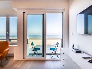A modern room with a large sliding glass door leading to a balcony with beach views. There is a desk with a computer and a TV mounted on the wall. - Apartment on Zeedijk With Stunning Sea View (Koksijde)