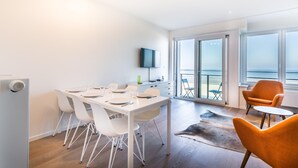 A modern living room with a dining area, large windows, and a view of the ocean. - Apartment on Zeedijk With Stunning Sea View (Koksijde)