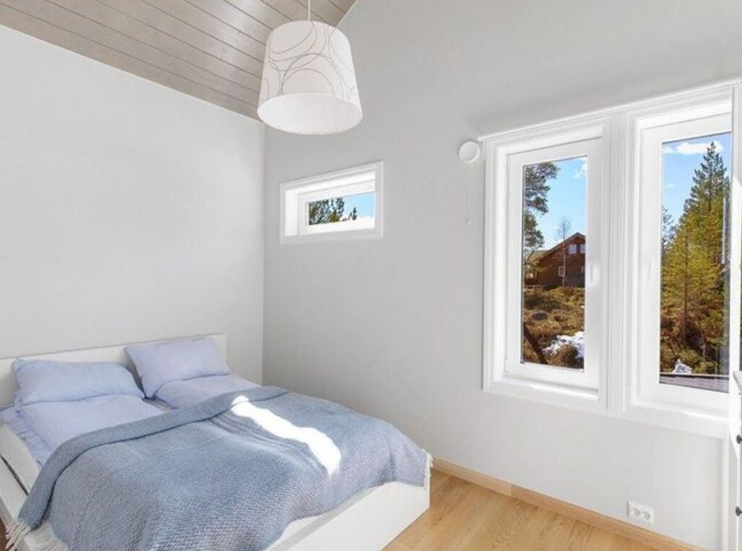 A bedroom with a bed, a window with a view of trees and a building, and a ceiling light fixture.