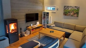 Ett modernt vardagsrum med en vedeldad kamin, en platt-TV, en soffa, ett soffbord och en bokhylla.