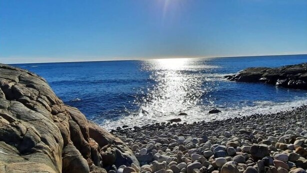 En stenstrand med havet och en klar himmel.