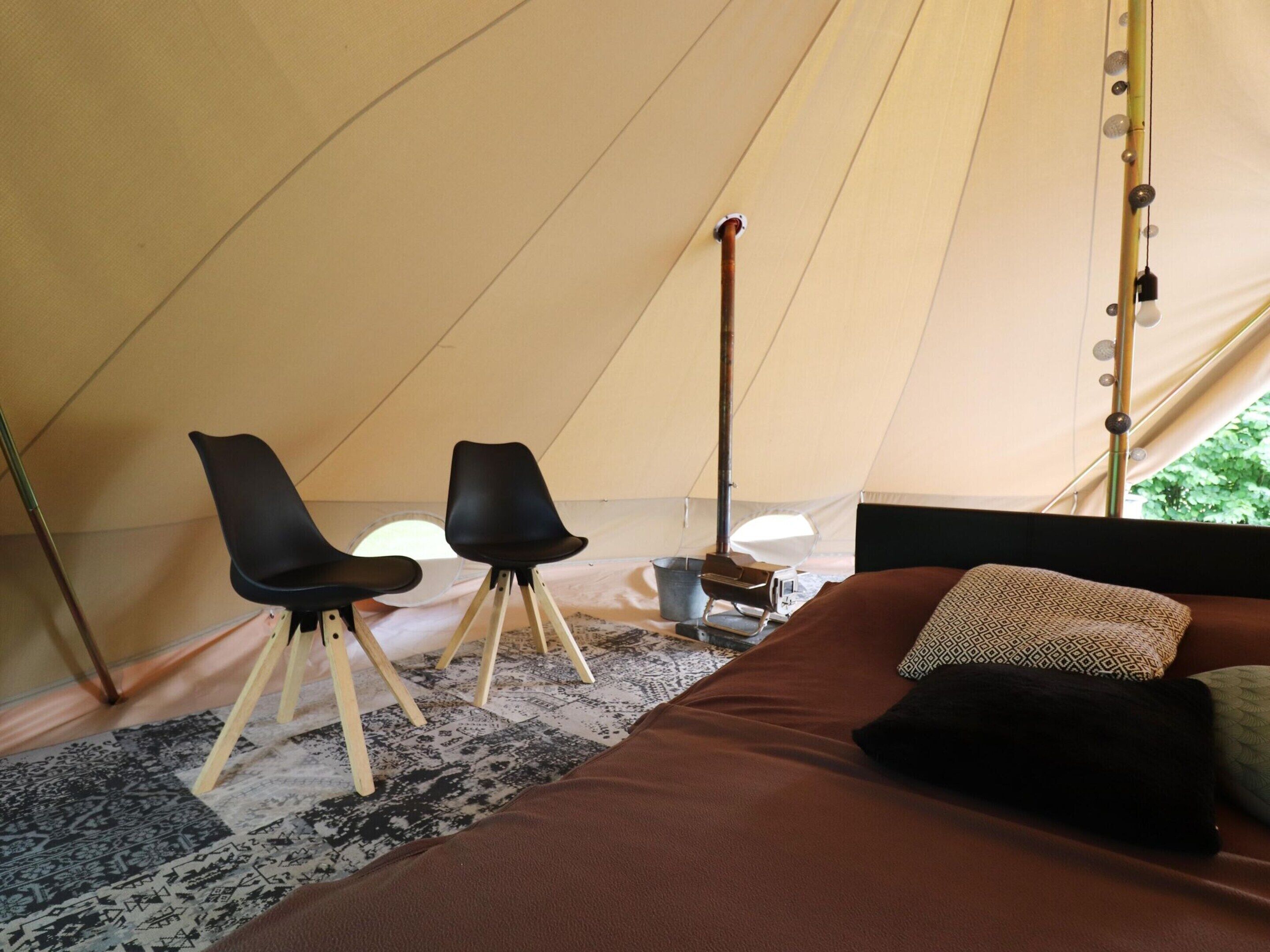 A tent with a bed, two chairs, and a lamp.