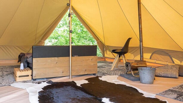 A tent interior with a wooden bench, a chair, a metal bucket, and a cowhide rug. - Tent Lodge in Twijzel Near Town Center (Twijzel)
