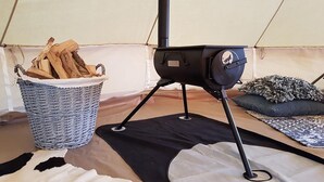 A portable stove with a basket of wood, a black mat, and a patterned rug inside a tent. - Tent Lodge in Twijzel Near Town Center (Twijzel)