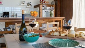 A kitchen with a wooden table, a bottle of wine, glasses, bread, and a bowl of olives. - Pool House Giulia Comfortable Holiday Residence (Letojanni)