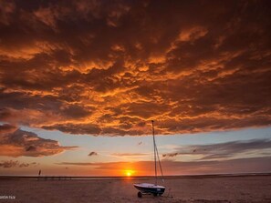 A boat on a sandy beach with a sunset in the background.