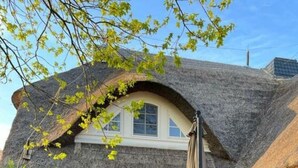 A house with a thatched roof, a red exterior, and a small patio area with a table and chairs. - Holiday Apartment Uhlenhof 1 (Mönchgut-Granitz)