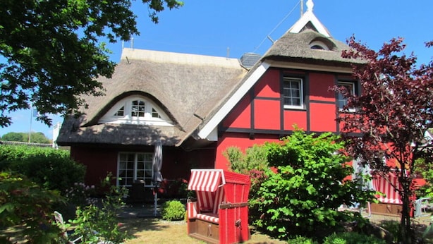A traditional red house with a thatched roof and a small red and white striped chair in the garden. - Holiday Apartment Uhlenhof 1 (Mönchgut-Granitz)