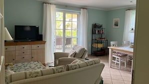 A room with a sofa, a TV, a bookshelf, and a dining area. - Holiday Apartment Uhlenhof 1 (Mönchgut-Granitz)