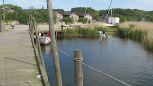 A wooden dock with boats, a small building, and a grassy area with trees in the background. - Holiday Apartment Uhlenhof 1 (Mönchgut-Granitz)