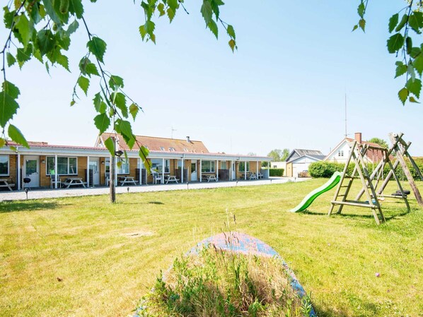 A building with a covered patio area, outdoor seating, and a playground with a slide. - Seaside Retreat in Kegnaes - By Traum Ferienwohnungen (Sydals)