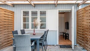 A covered patio area with a table and chairs, a window with a view, and a door leading inside. - Seaside Retreat in Kegnaes - By Traum Ferienwohnungen (Sydals)