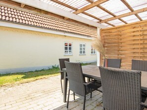 An outdoor patio with a table and chairs, a pergola, and a building with a tiled roof in the background. - Seaside Retreat in Kegnaes - By Traum Ferienwohnungen (Sydals)