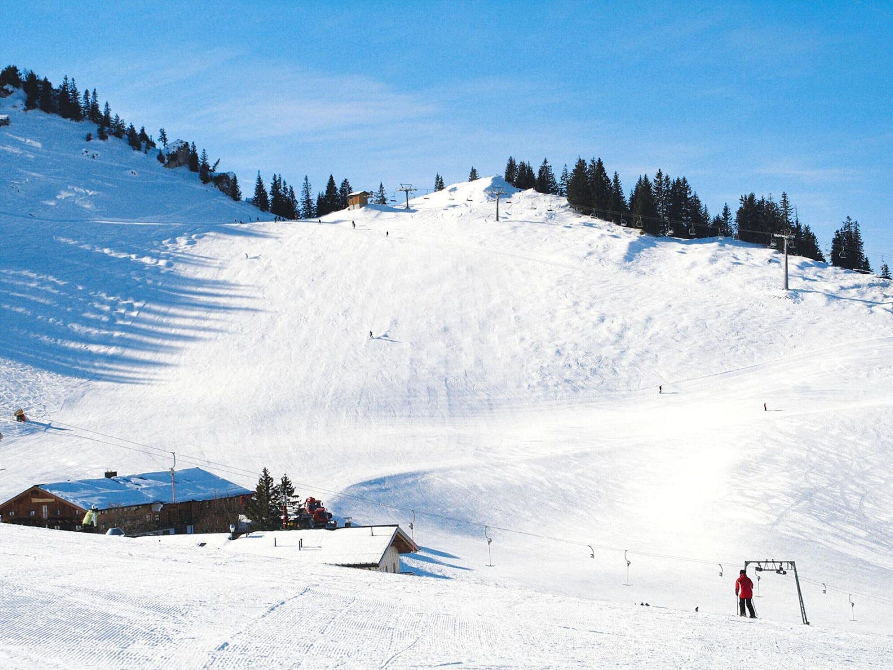 A snow-covered ski slope with a ski lift, a wooden cabin, and a clear blue sky.