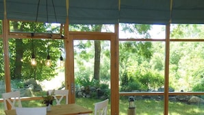 Une table à manger en bois, entourée de chaises blanches, de grandes portes vitrées et offrant une vue sur un paysage verdoyant.