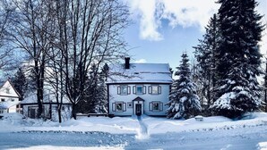 Una casa de dos pisos con un camino de entrada cubierto de nieve y árboles circundantes.