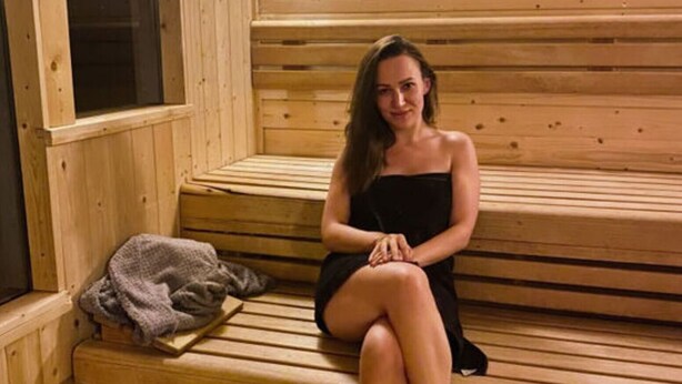 Una persona sentada en bancos de madera dentro de un sauna, con una ventana y una toalla sobre el banco.