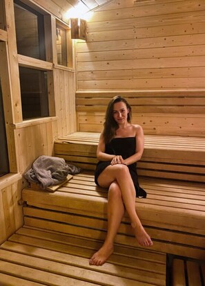 Uma pessoa sentada em bancos de madeira em um salão de sauna, com uma janela e uma toalha no banco.