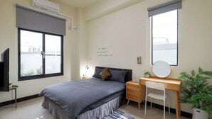 Une chambre à coucher comprenant un lit, une table de chevet, un bureau, une chaise et une plante en pot.