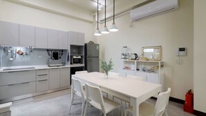 Une cuisine moderne avec des meubles blancs, une table à manger avec des chaises et une machine à café.