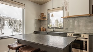 A modern kitchen with a large island, stainless steel appliances, and a view of a snowy landscape.