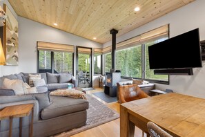 A modern living room with a fireplace, large windows, a television, and a dining area.