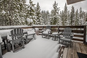 An outdoor deck with wooden chairs and tables covered in snow, surrounded by snow-covered trees.