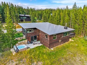 A modern cabin with a metal roof, a hot tub, and a deck with outdoor furniture.