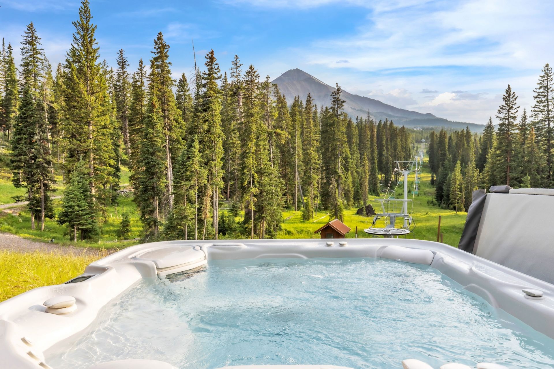 Un jacuzzi con vistas a la montaña, rodeado de un bosque y una cabaña pequeña.