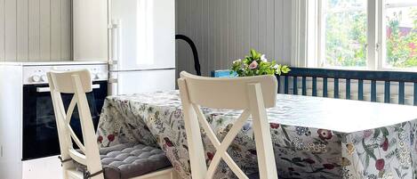 A compact kitchen with a refrigerator, oven, and a dining table with floral tablecloths.